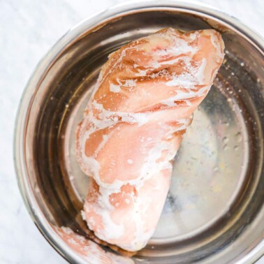 a big chunk of frozen chicken breast in the stainless steel pot of an instant pot