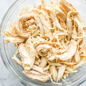 a clear glass bowl of shredded chicken sitting on a marble surface
