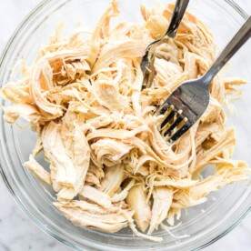 shredded chicken in a clear glass bowl on a marble surface