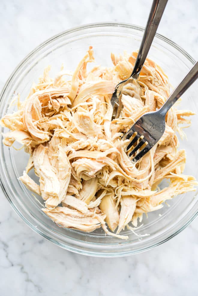 shredded chicken in a clear glass bowl on a marble surface