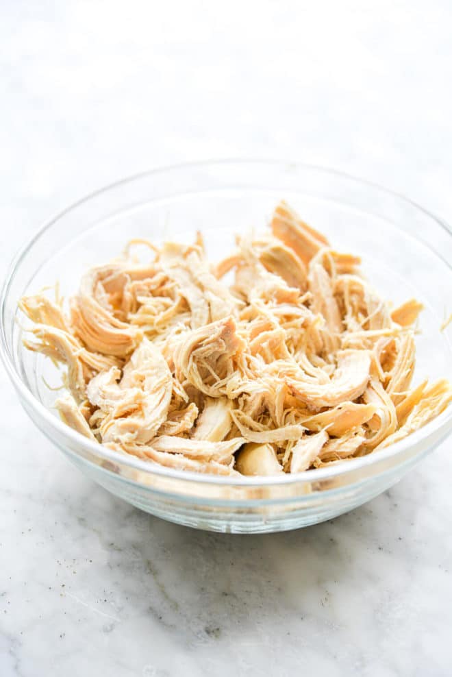 shredded chicken in a clear glass bowl on a marble surface