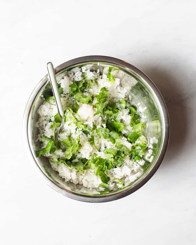 a metal bowl of white rice mixed with cilantro leaves