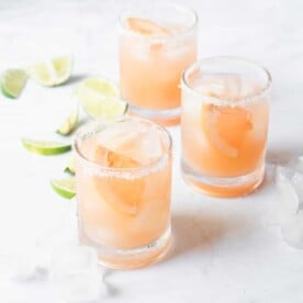 a salt rimmed glass of palomas sitting on a marble surface