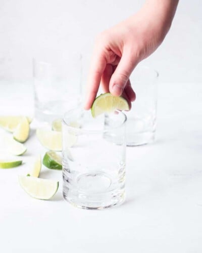 a person's hand squeezing lime juice over the rim of a glass