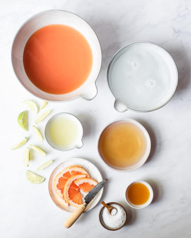 all of the ingredients for pitcher palomas in different sized containers on a marble surface