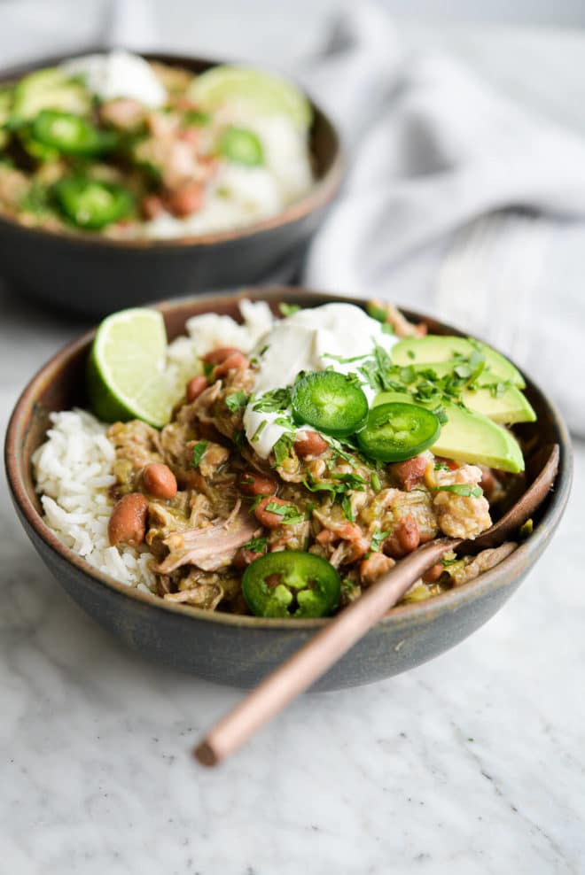 two bowls of pork chili verde over white rice on a marble surface