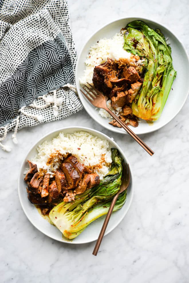 two shallow bowls of white rice, teriyaki pork tenderloin, and bok choy