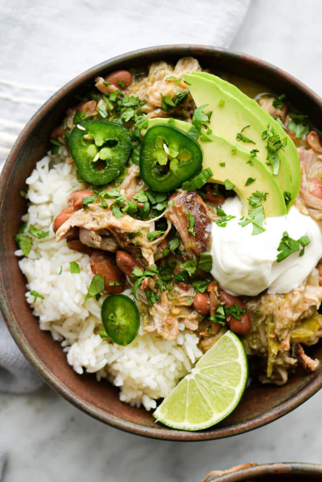 a bowl of pork chili verde over white rice on a marble surface