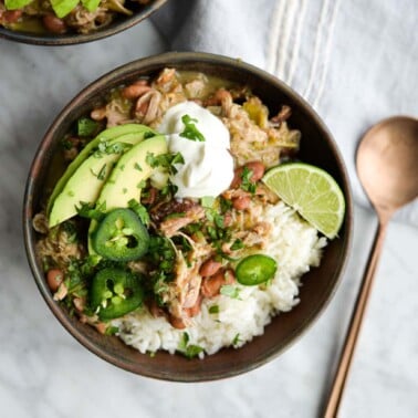 two bowls of pork chili verde over white rice on a marble surface