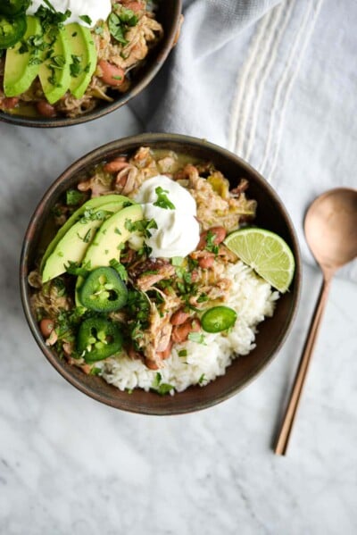 two bowls of pork chili verde over white rice on a marble surface