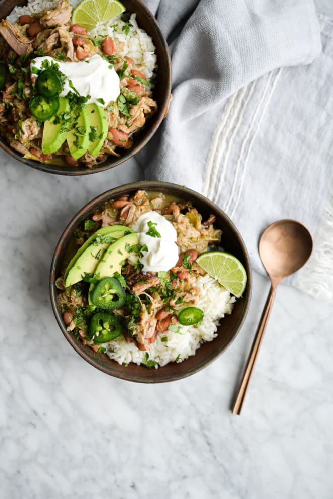 two bowls of pork chili verde over white rice on a marble surface