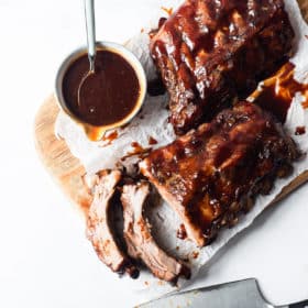 two half racks of ribs smothered in BBQ sauce sitting on a wooden cutting board next to a bowl of more BBQ sauce