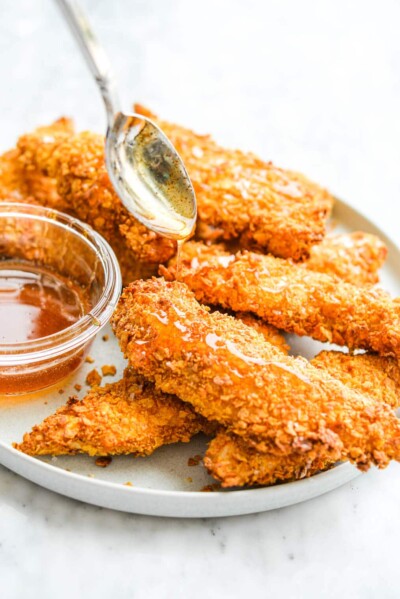 a plate of crispy air fryer chicken tenders with hot honey sauce being drizzled over them