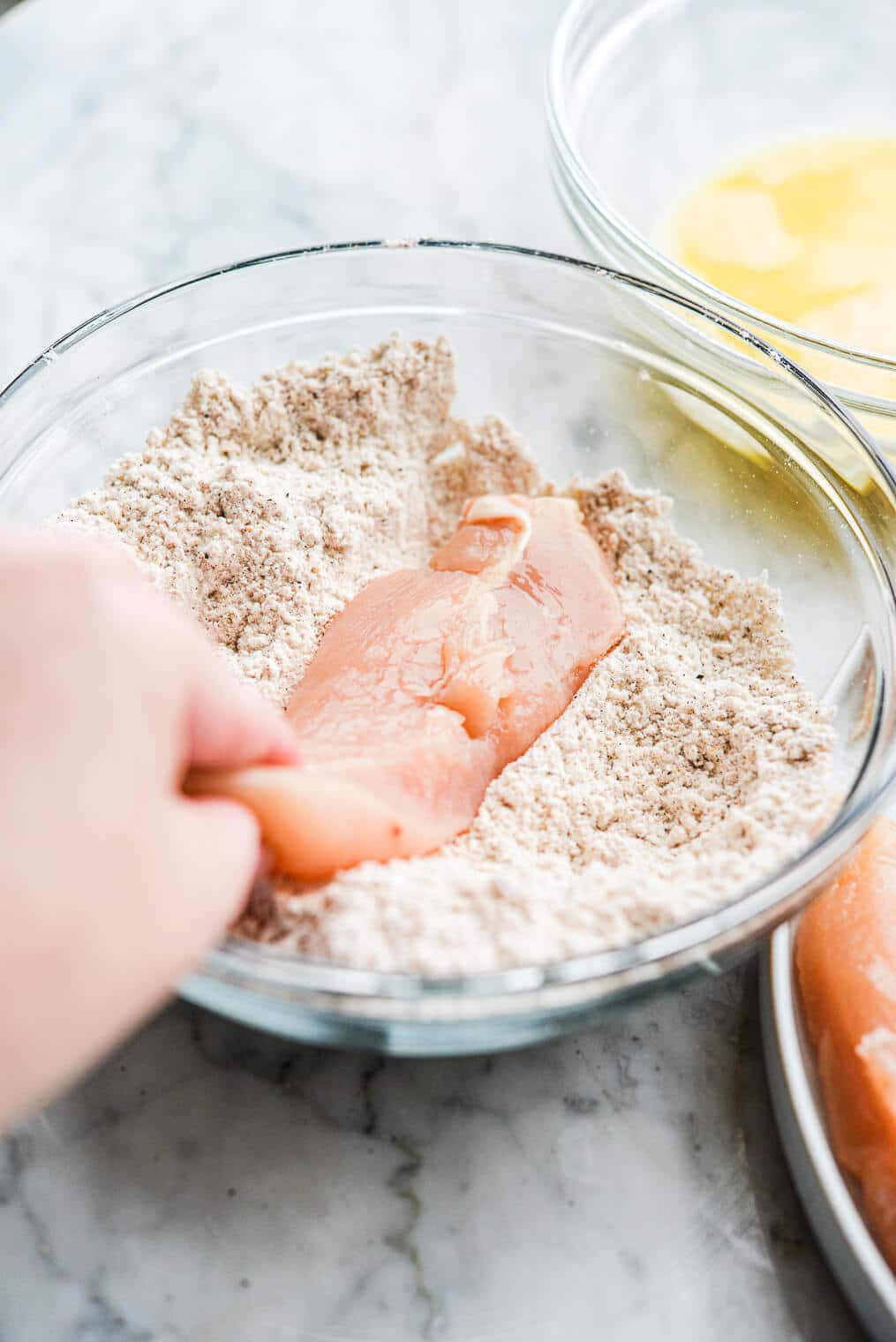 a person coating a raw chicken tender in a flour mixture