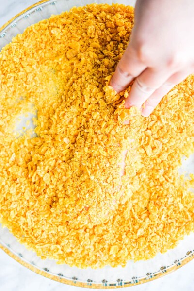 a person coating a raw chicken tender in crushed cornflakes