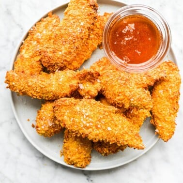a plate of crispy air fryer chicken tenders on a plate next to a small clear bowl of hot honey dipping sauce