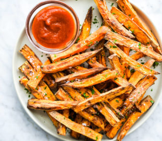 a plate of crispy sweet potato fries next to a small glass bowl of ketchup