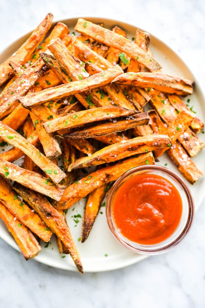 a plate of crispy sweet potato fries next to a small glass bowl of ketchup