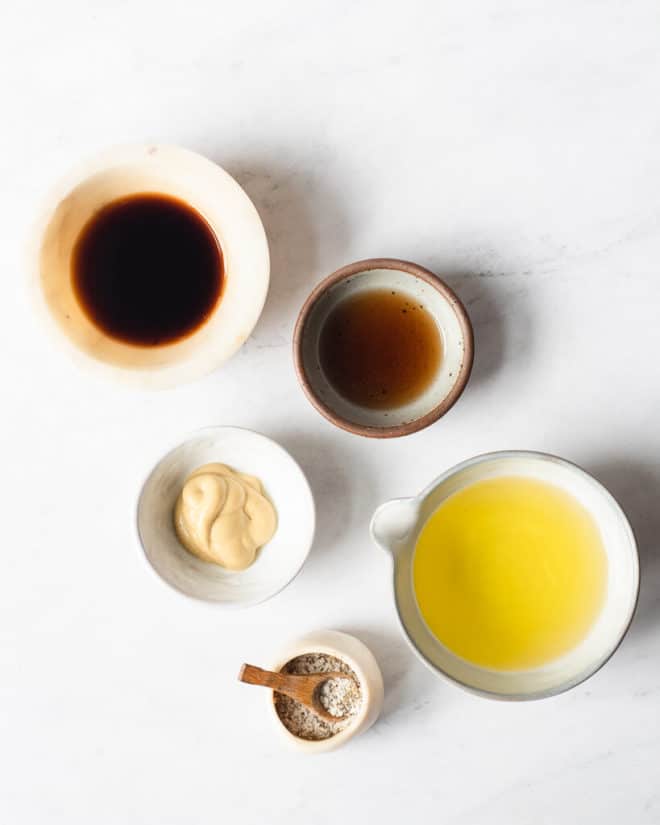 the ingredients for homemade balsamic vinaigrette in different sized bowls sitting on a marble surface