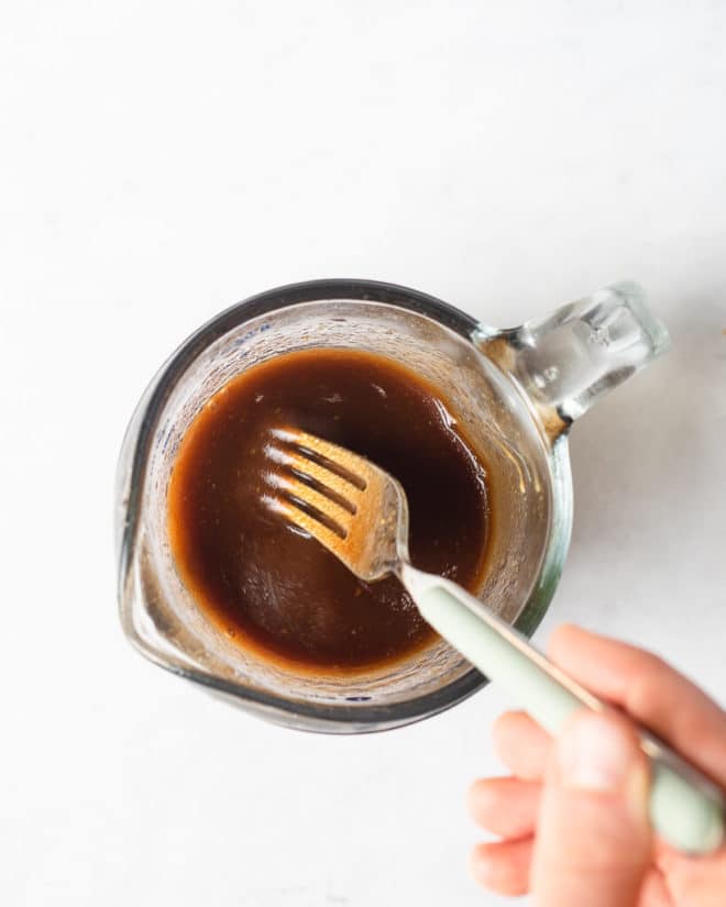 a person using a fork to whisk together a homemade balsamic vinaigrette dressing in a spouted measuring cup