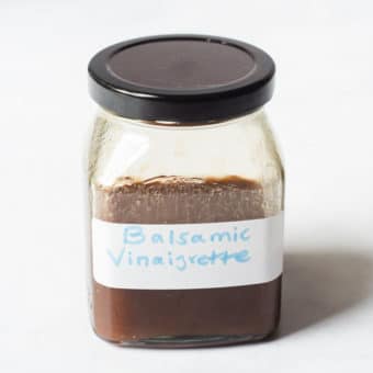 a clear glass jar with a black screw on lid filled with a brown liquid labeled "balsamic vinaigrette"