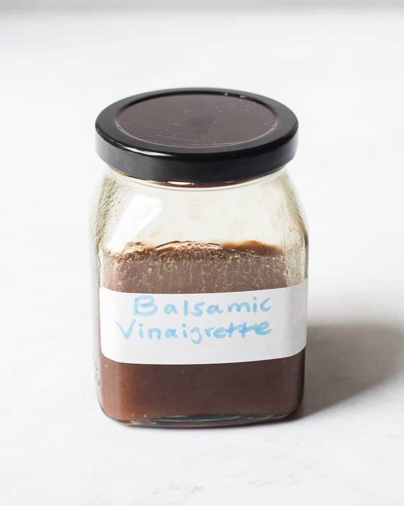 a clear glass jar with a black screw on lid filled with a brown liquid labeled "balsamic vinaigrette"