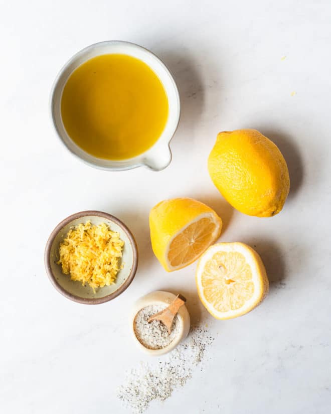 the ingredients needed for lemon vinaigrette in different sized bowls on a marble surface