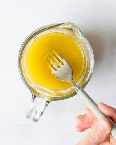 a person whisking together the ingredients for lemon vinaigrette in a spouted measuring cup