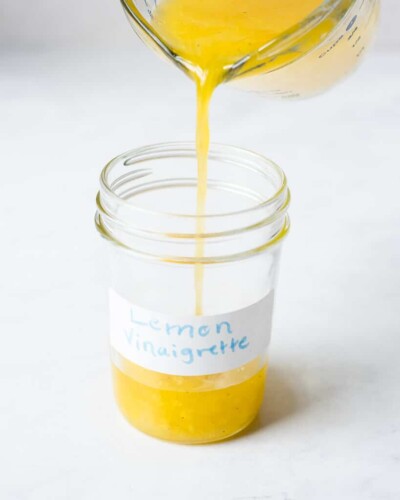 someone pouring lemon vinaigrette from a large spouted measuring cup into a small mason jar