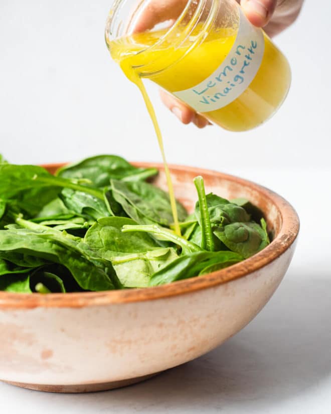 a wooden bowl filled with spinach being drizzled with lemon vinaigrette