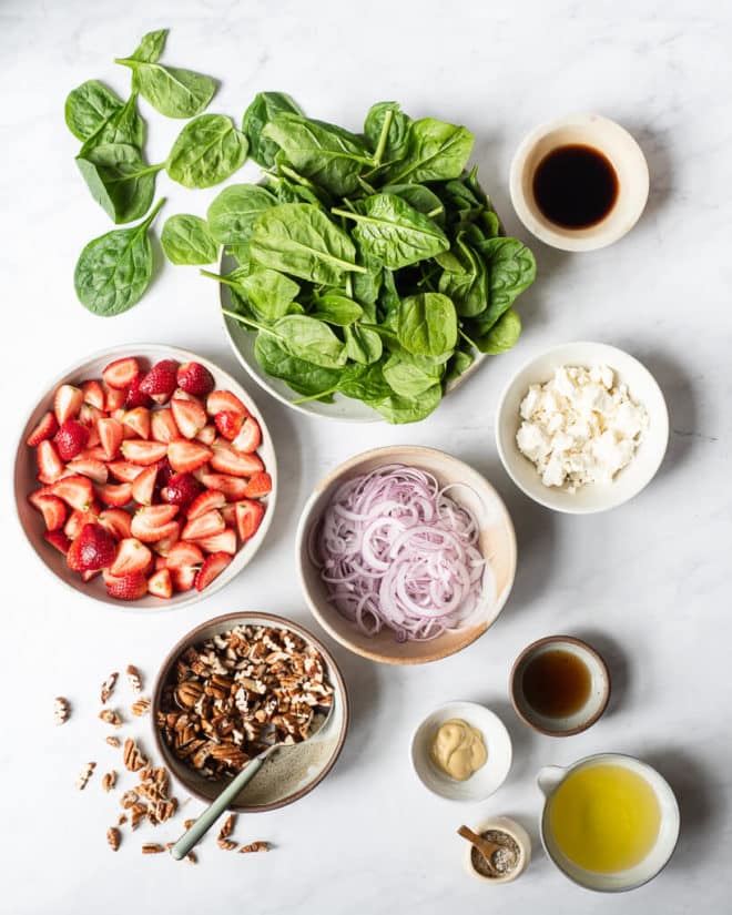 the ingredients for strawberry spinach salad (spinach, pecans, strawberries, goat cheese, red onion, and dressing ingredients)