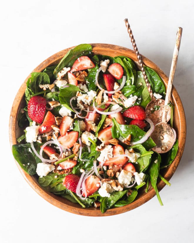 a large wooden bowl of strawberry spinach salad with two large spoons sticking out of it