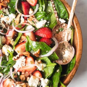 a large wooden bowl of strawberry spinach salad with two large spoons sticking out of it