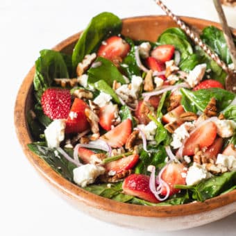 a large wooden bowl of strawberry spinach salad with two large spoons sticking out of it