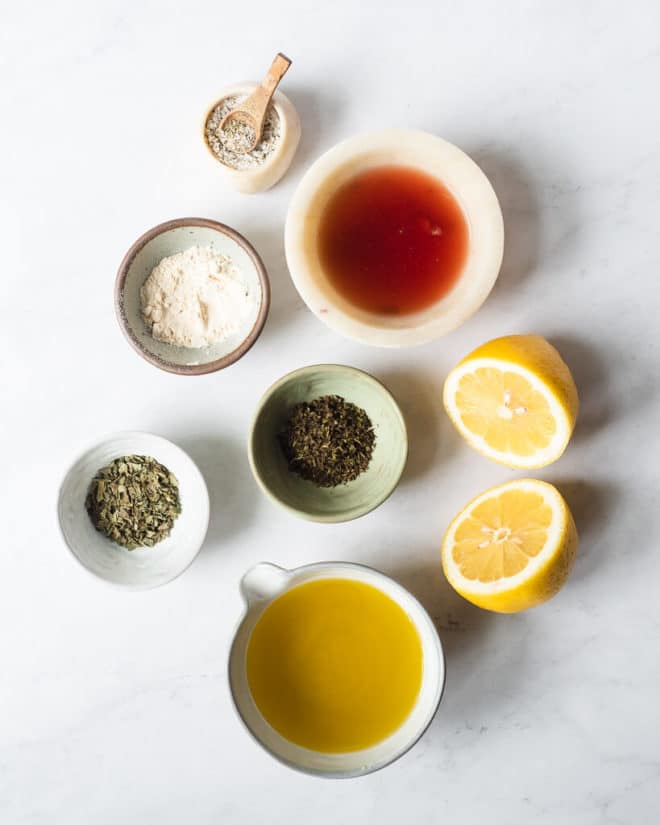 all of the ingredients for homemade Greek dressing in different sized bowls and plates on a marble surface