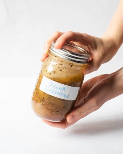 a person holding a mason jar of homemade Greek dressing with both hands