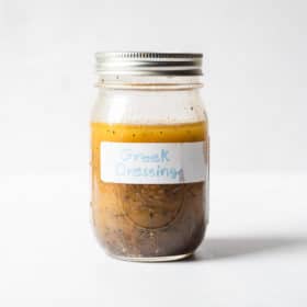 a mason jar of homemade Greek dressing sitting in front of a white background