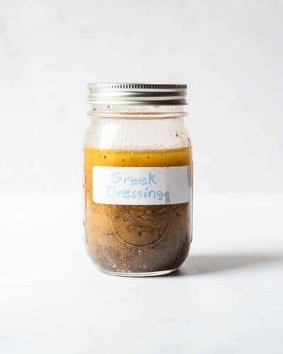 a mason jar of homemade Greek dressing sitting in front of a white background