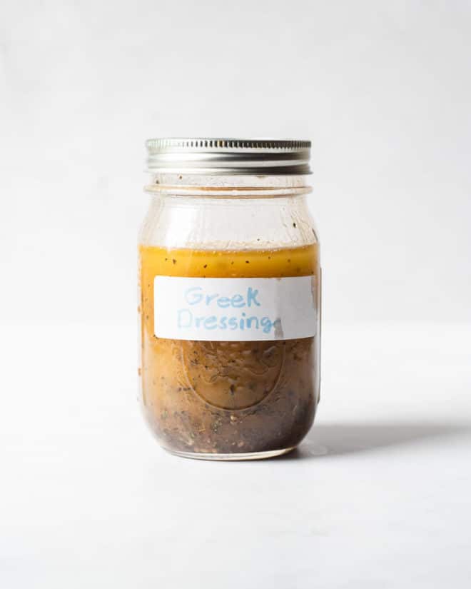 a mason jar of homemade Greek dressing sitting in front of a white background
