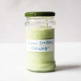 a labeled jar of homemade green goddess dressing sitting in front of a white background