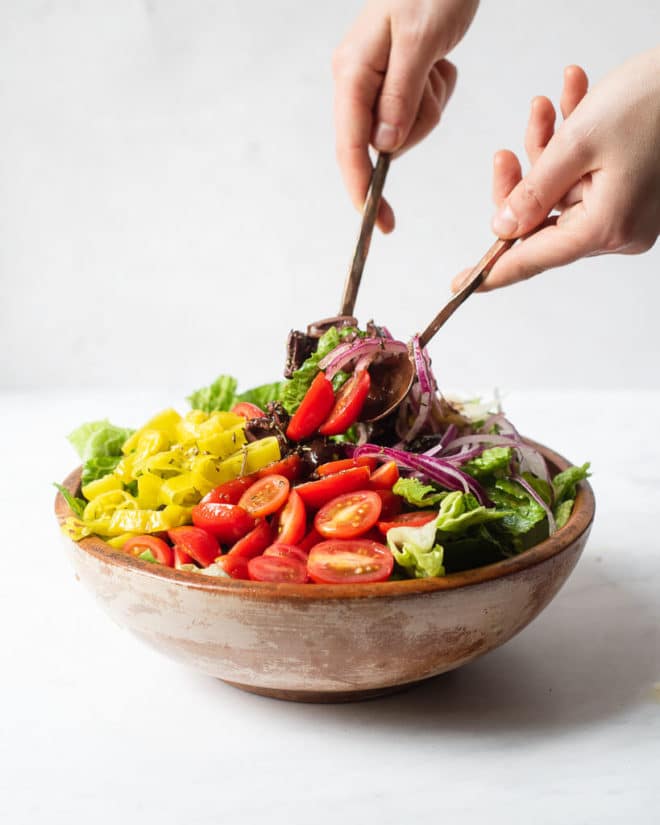 an italian salad loaded with red onions, parmesan cheese, cherry tomatoes, and olives sitting in a bowl