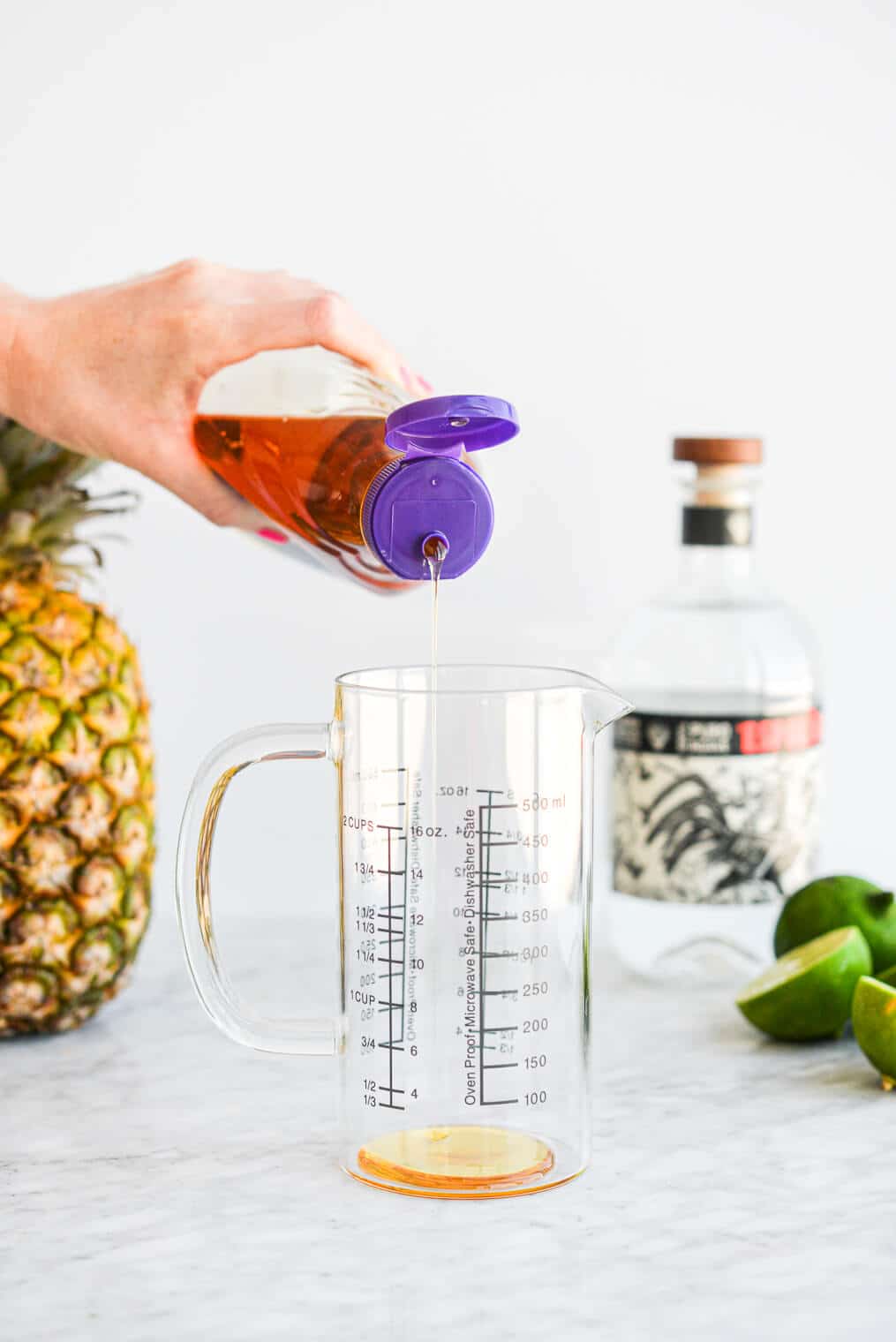 a person squeezing agave nectar into a large glass measuring cup