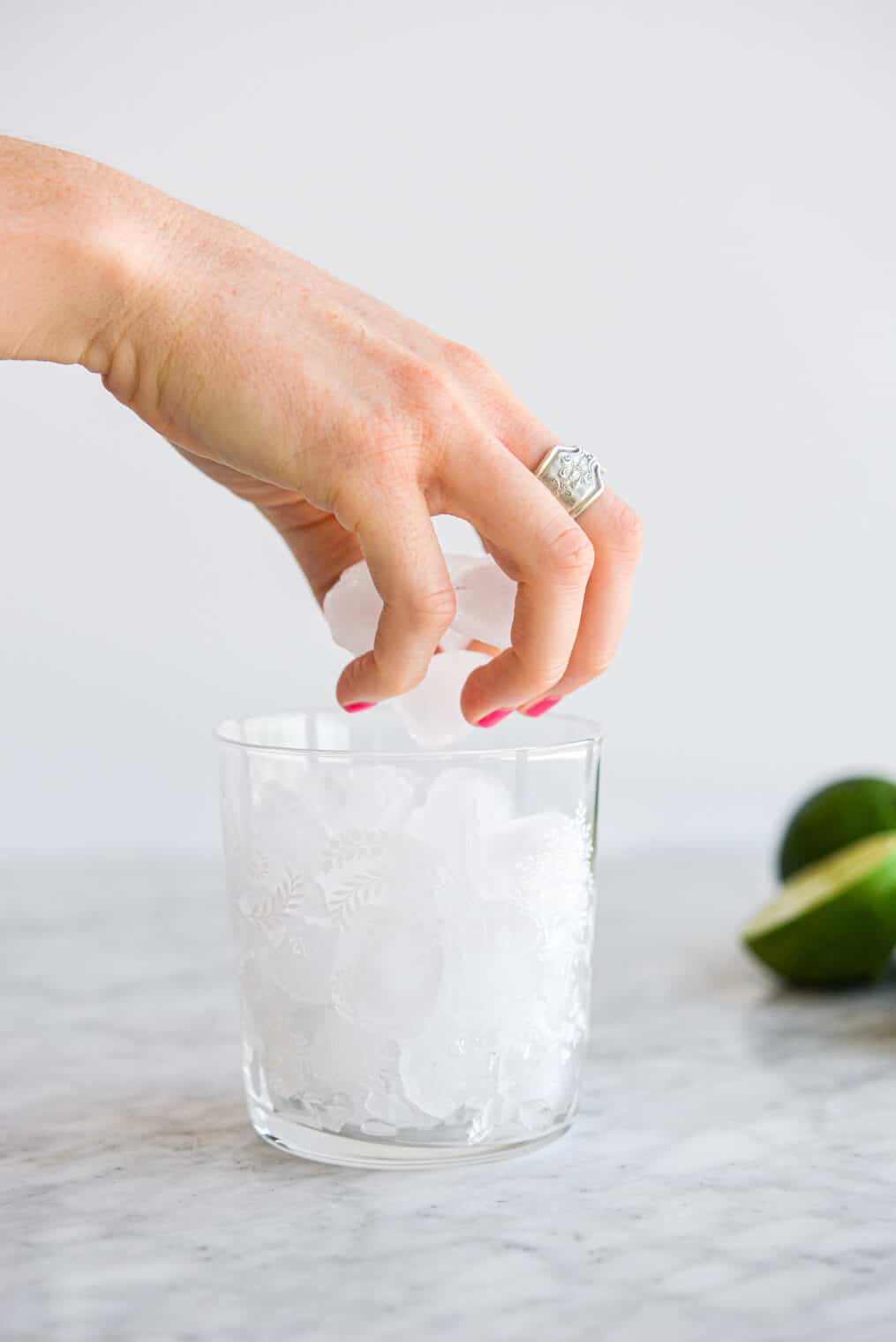 a person putting ice cubes into a small margarita glass