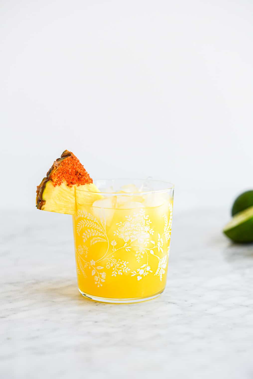 a margarita glass with a pineapple margarita on the rocks in it garnished with a pineapple wedge dipped in chili salt