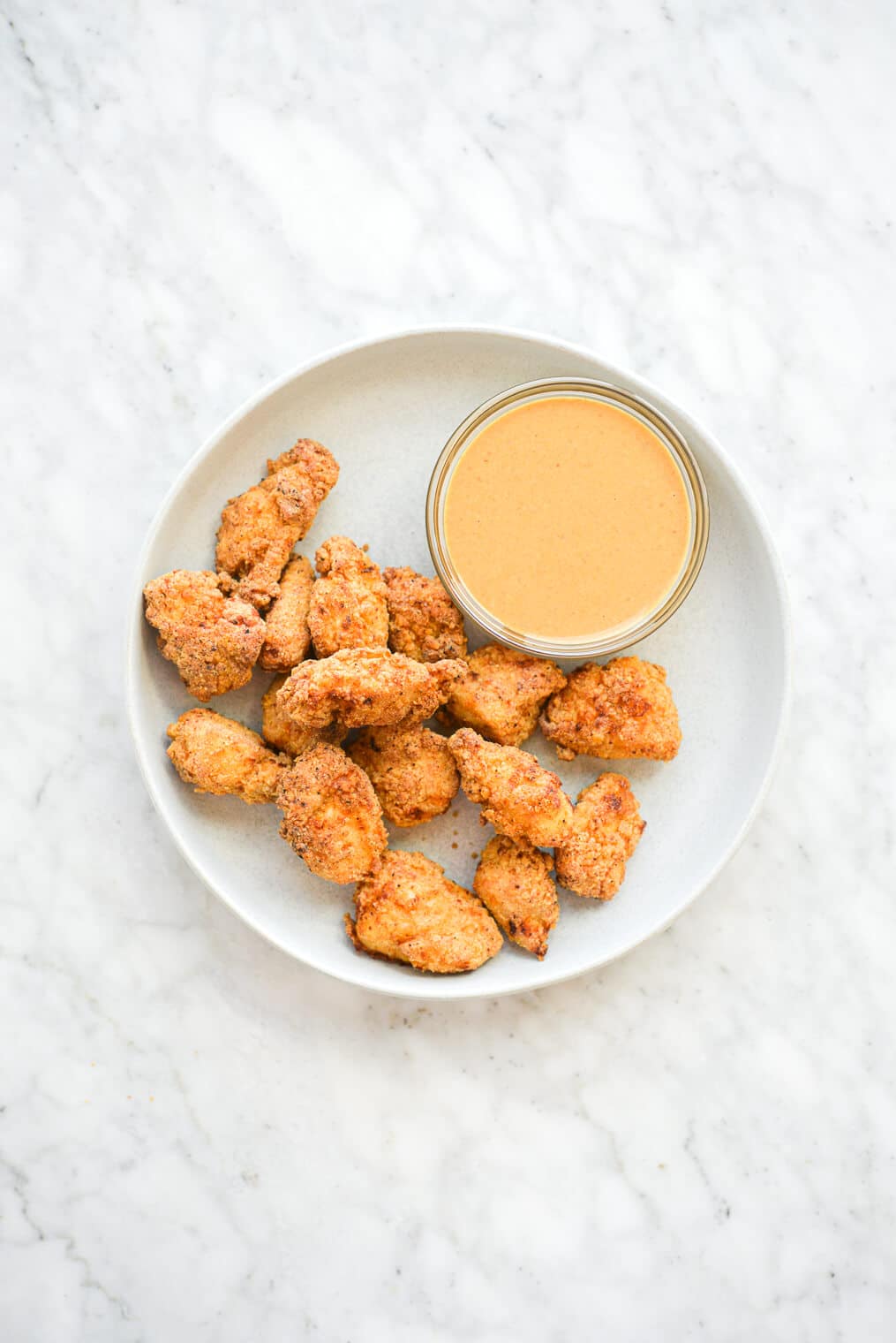 a plate of air fryer chicken nuggets next to a small glass bowl of an orange sauce