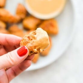 a person's hand holding a chicken nugget that has been dipped in a orange sauce