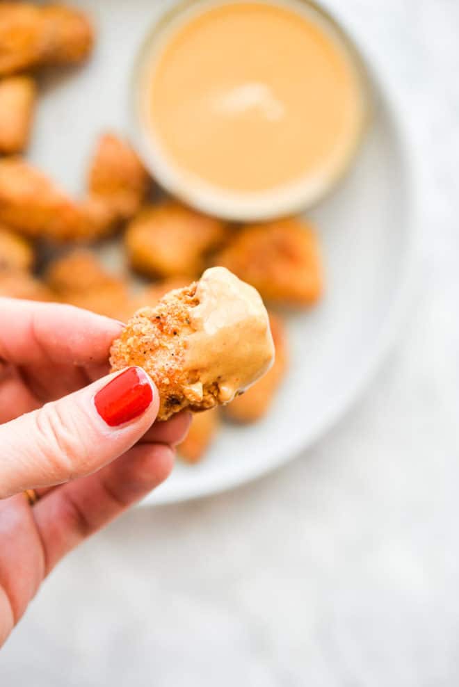 a person's hand holding a chicken nugget that has been dipped in a orange sauce