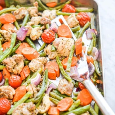 a sheet pan of chicken thighs and veggies with a spatula scooping up a serving of it