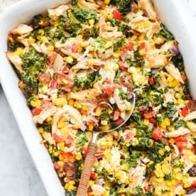a casserole dish of confetti chicken casserole with a large spoon scooping out a serving of it