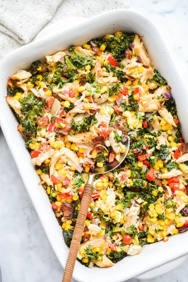 a casserole dish of confetti chicken casserole with a large spoon scooping out a serving of it